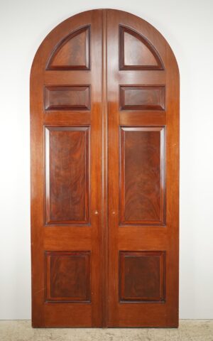 Arched double doors with four panels each, shown in a dark wood finish with a central seam and minor surface wear visible.