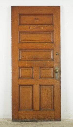 Antique chestnut entry door with seven panels and attached brass hardware, shown full length with visible surface wear.