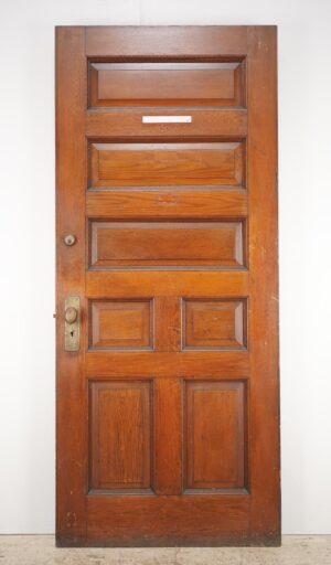 Antique chestnut entry door with seven panels, right-hand inswing, showing original brass and steel hardware and surface wear.