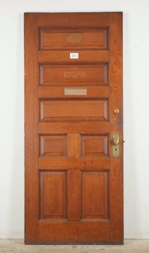 Antique seven-panel entry door in a dark wood tone with original brass and steel hardware, shown front on with visible surface wear and a number plate.