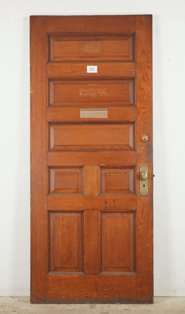 Antique seven-panel entry door in a dark wood tone with original brass and steel hardware, shown front on with visible surface wear and a number plate.