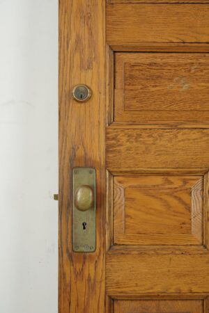 Close-up of a chestnut wood entry door showing the lockset and keyhole, with seven-panel detailing and visible surface wear in the finish.