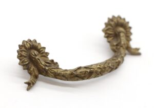 Pair of antique brass drawer pulls with a floral swag bridge design shown in close-up from the front, with one handle end in focus and the other blurred.