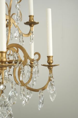 Close-up of a French Louis style chandelier with an antique bronze frame, white candle sleeves, and dangling clear crystal teardrops and pendeloques.