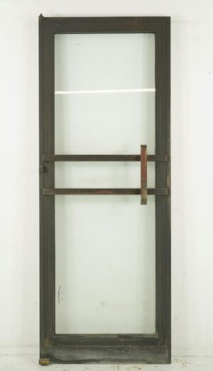 Art Deco commercial door with a full glass panel, bronze frame, and two horizontal pull bars, shown front on with visible surface wear and a cracked glass area.