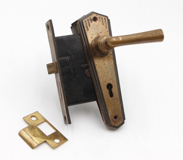 Art Deco passage door knob set with a brass lever, brass back plates, and a strike plate shown in a close-up view.