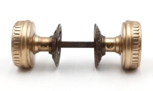 Side view of two antique brass door knobs from an 1880s passage set, shown connected by the original metal spindle.