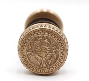 Ornate brass stamp, top view showing a central star and intricate 1880s-inspired patterns around the circular edge.