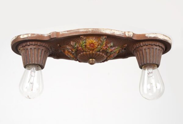 Art Deco flush mount light with two exposed bulbs, fluted sockets, and raised floral detail on a darkened bronze cast iron base.