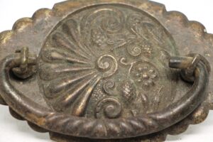 Victorian brass drawer bail pull with an ornate floral backplate and aged patina, shown in close-up.