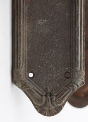 Close-up of an Art Nouveau bronze back plate with aged dark patina, a pointed bottom edge, and two mounting holes.