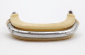 Mid Century drawer pull with an ivory plastic handle and nickeled brass base, shown in close-up with visible surface wear.