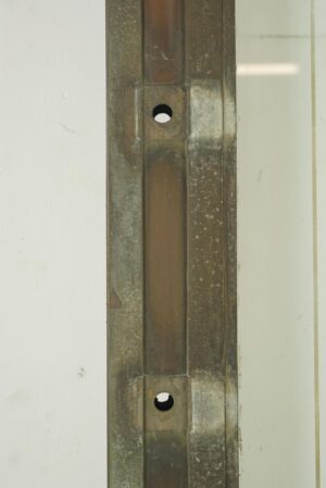 Close-up of an antique bronze door frame with two circular hinge pockets and surface wear visible along the vertical edge.