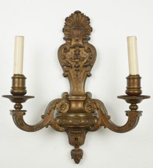 Ornate bronze two-arm wall sconce with classical scrollwork, acanthus leaves, and two candle sockets.