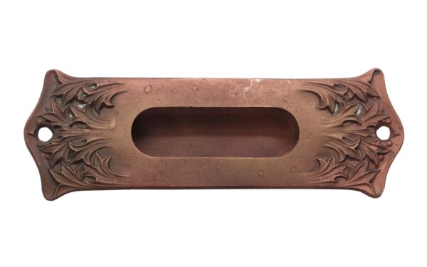 Art Nouveau bronze window sash lift with an antique finish and decorative floral scrollwork, shown front view with two mounting holes and a recessed handle opening.