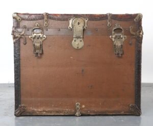 Antique travel trunk with brown wood, leather binding, and aged nickel hardware, shown closed with surface wear and a central latch.