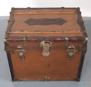 Antique travel trunk made of brown painted wood bound in leather, shown closed with nickel-finish steel hardware and visible surface wear.