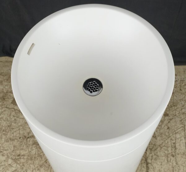 Top view of a white round pedestal sink with a chrome drain cover and overflow hole visible in the basin.