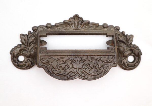 Victorian cast iron drawer pull with an ornate apothecary design and a label slot opening.