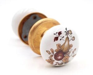 Vintage passage door knob set with white porcelain knobs, a brown and tan fruit motif, and polished brass rosettes.