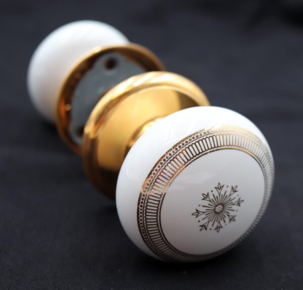 Two white ceramic passage door knobs with gold snowflake motifs and polished brass rosettes are shown in a close-up view.