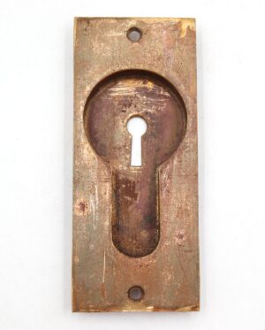 Vintage brass recessed pocket door pull with a classic rectangular plate and keyhole cutout, shown front on with visible surface wear and mounting holes.