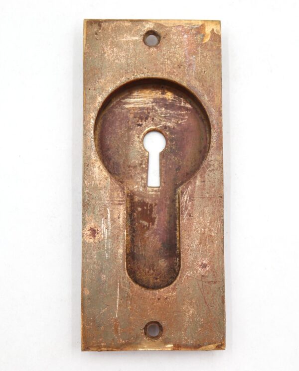 Vintage brass recessed pocket door pull with a classic rectangular plate and keyhole cutout, shown front on with visible surface wear and mounting holes.