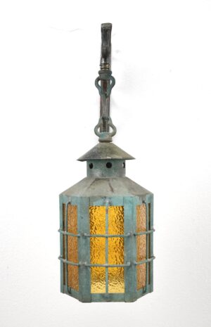 Vintage wall-mounted lantern with a copper frame, textured amber glass panels, and a bronze hanging bracket, shown with surface wear and a crack in one panel.