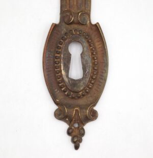 French-style brass door back plate with a central keyhole opening and ornate oval detailing, shown front-on.