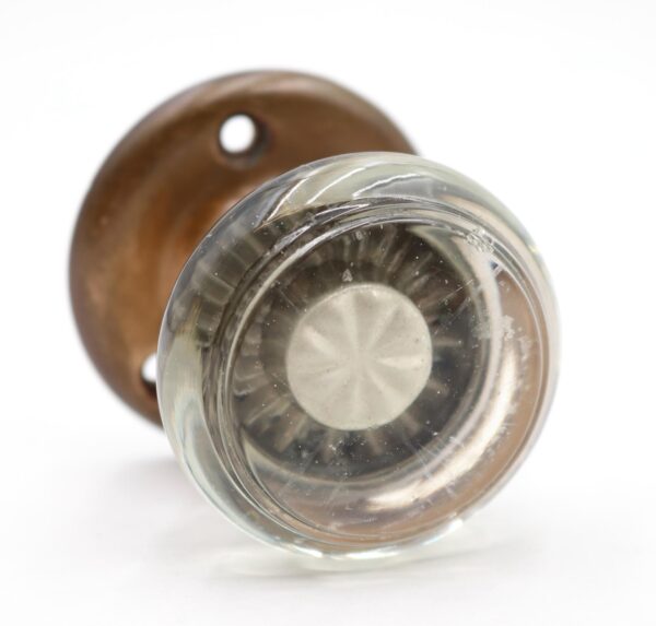 Close-up of a clear glass door knob with an antique brass rosette and mounting holes visible behind it.
