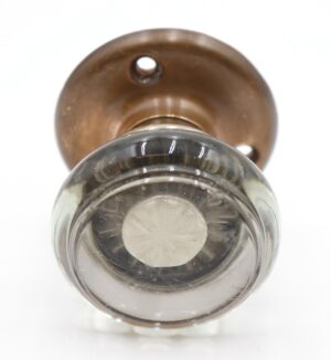 Round clear glass door knob with an antique brass rosette and visible mounting holes, shown from the front.
