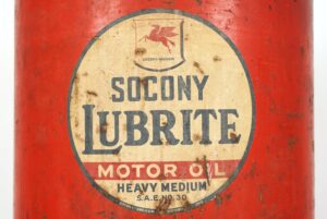 Close-up of a vintage oil dispenser label on a red steel container, showing Socony Lubrite motor oil, Heavy Medium, and worn tan and black graphics.