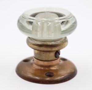 Antique Art Deco round clear glass door knob with an antique brass rosette and dummy spindle, shown in close-up view.
