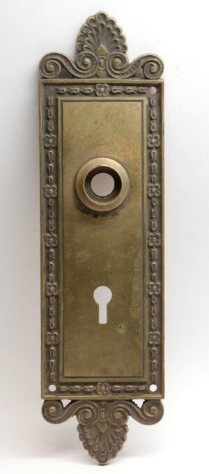 Neoclassical bronze entry back plate with ornate scroll and fan details, a keyhole opening, and a circular cylinder hole in the center.