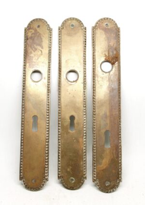 Set of three French passage door back plates with beaded edges, each shown front on with keyhole and round opening, displaying surface wear and an antique bronze finish.