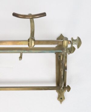 Vintage brass luggage rack with a curved top rail, several hooks, and a wall-mount bracket visible on the right side.