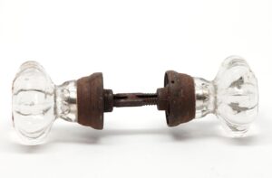 A pair of clear glass door knobs with rusted cast iron shanks and a spindle.