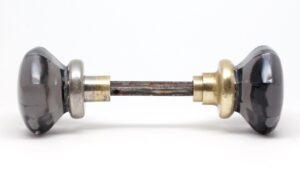 Pair of purple glass door knobs with a spindle, shown in side view with nickel and polished brass shanks.