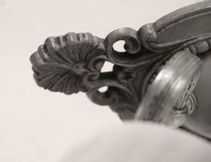 Close-up of a two-light wall sconce with ornate foliage detail and a visible glass shade, shown in a nickel finish.