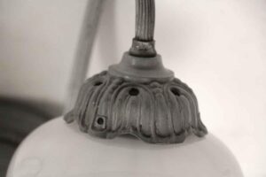 Close-up of a wall sconce mount with ornate foliage detail and a visible cord entering the top, shown in a nickel-plated finish.