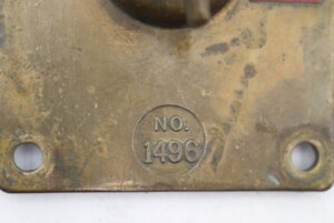 Close-up of an antique brass light switch plate stamped No. 1496, showing the lower mounting holes and worn surface.