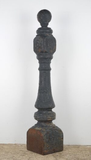 An antique Victorian cast iron newel post with a large ball finial, turned details, and worn black finish showing rust and chipped paint.
