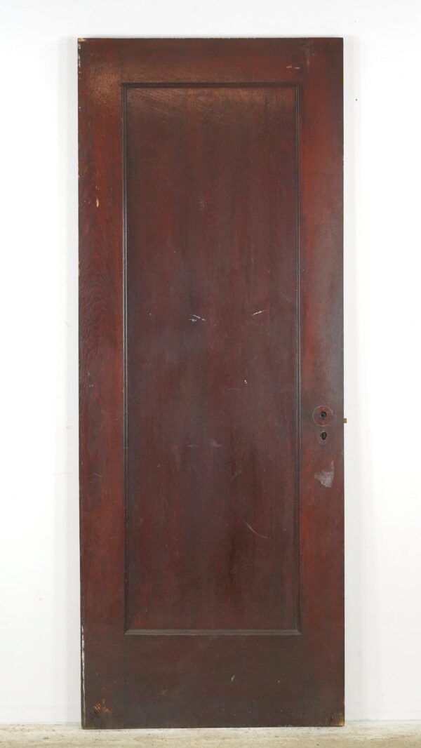 Vintage one-panel wood passage door with a dark wood tone, shown full length with heavy finish wear and the original mortise hardware visible on the right edge.