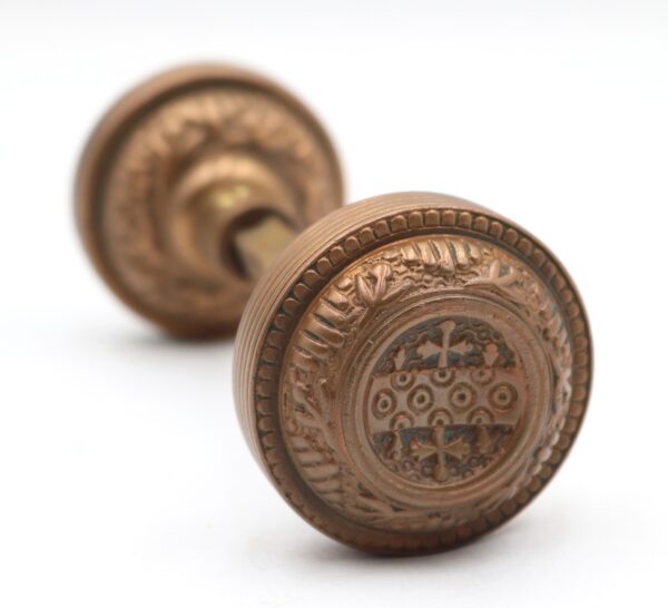 Pair of antique brass door knobs shown in close-up, with one ornate knob in front and the matching knob blurred behind it.