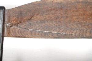 Close-up of a dark wood stadium seat slat attached to a black steel frame, showing a screw, visible cracks, and a long split in the wood.