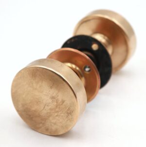 Brushed brass round flat door knob set shown in close-up with two knobs, two rosettes, and a spindle.