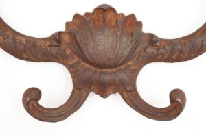 Victorian cast iron hall tree hook with four prongs and a heavily rusted surface shown in close-up.
