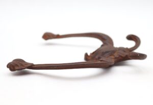 Victorian cast iron hall tree hook shown in close-up from the front, with four curved prongs and a heavily rusted surface.