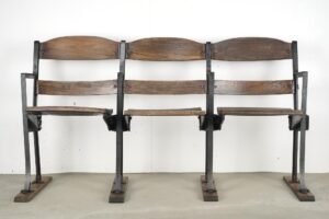 Three-seater folding stadium seats with dark wood slats and a black steel frame, shown front on with three attached seats and minor wear visible on the wood and metal.