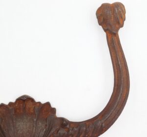 Close-up of a cast iron hall tree hook with a curved arm and ornate top and base in a heavily rusted black finish.